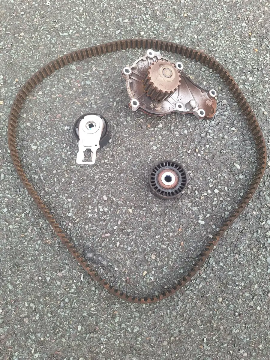 An old timing belt, tensioner, idler roller and water pump laid out after removal