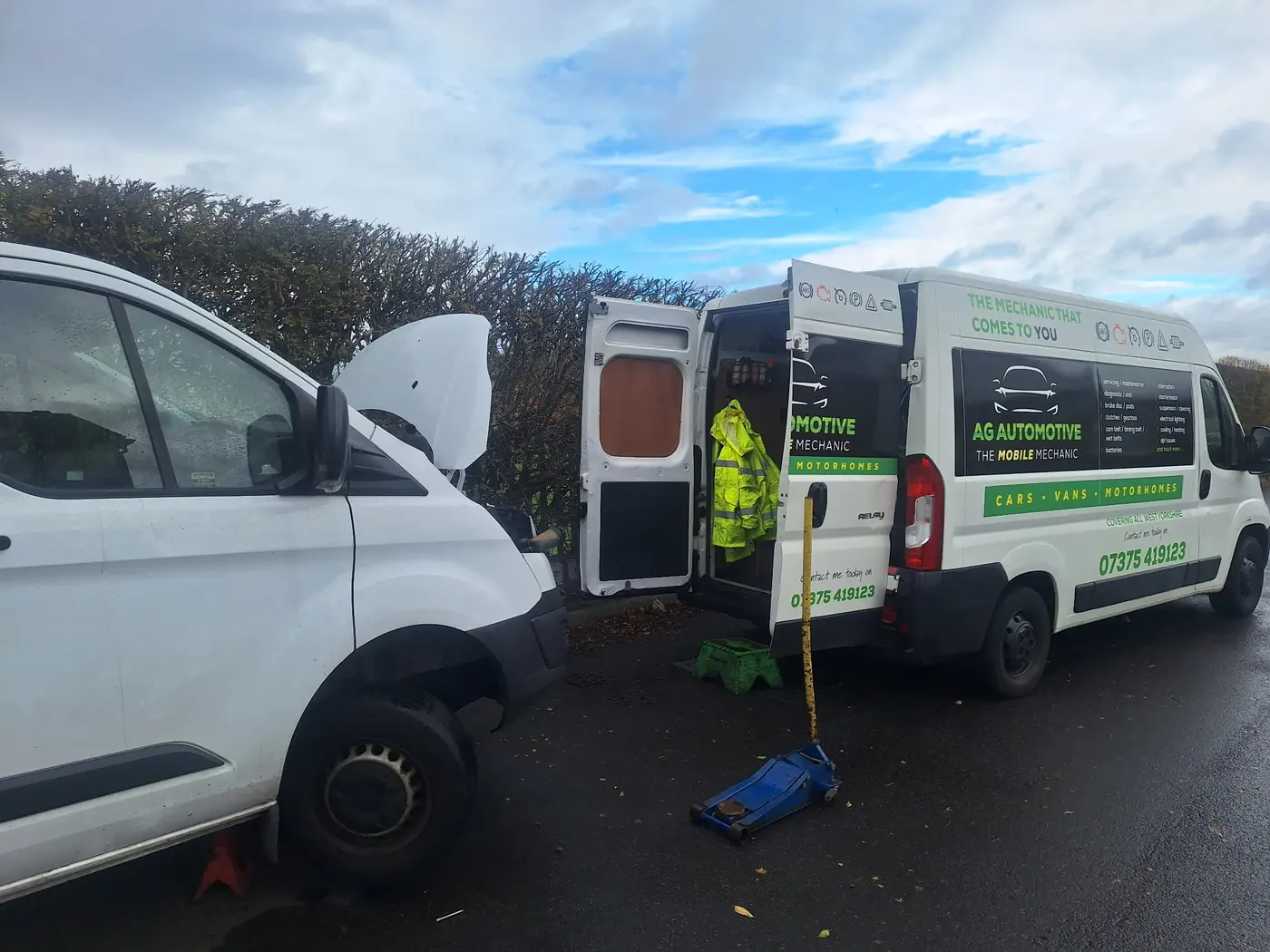 The AG Automotive van parked at a job with its rear doors open and tools inside